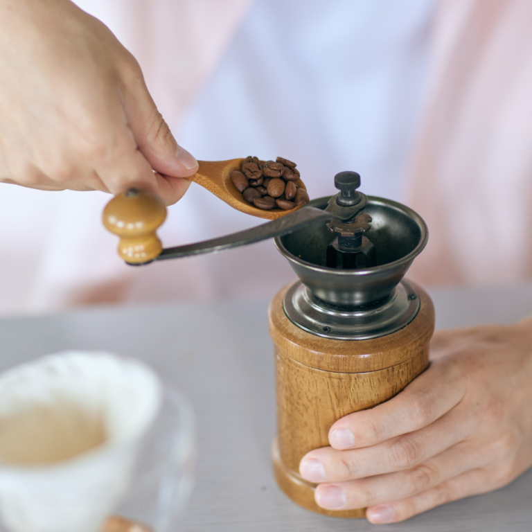 A woman grinding coffee with a manual coffee grinder